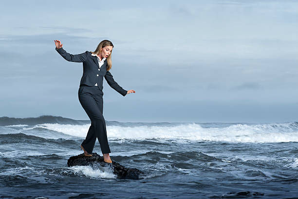 donna d'affari in equilibrio precariously su roccia nell'oceano - storm sea business uncertainty foto e immagini stock