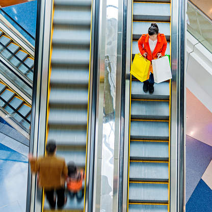 Female shopper standing on escalator with shopping bags in hand.