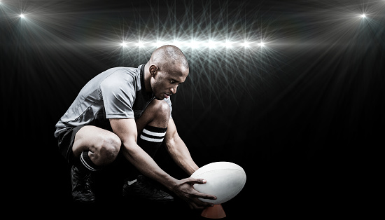 Rugby player keeping ball on kicking tee against spotlight