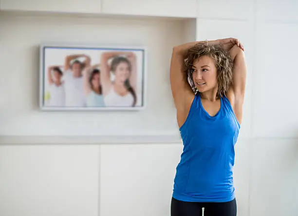 Young woman exercising at home watching tv - healthy lifestyle