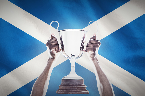 Cropped hand of athlete holding trophy against close-up of scottish flag