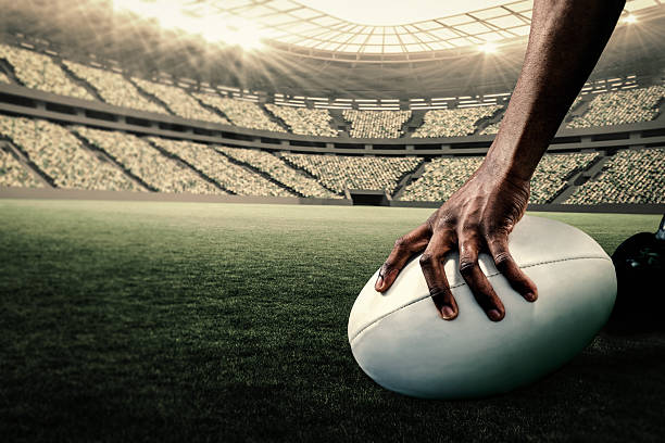 Composite image of rugby player holding ball Cropped image of athlete holding rugby ball against rugby stadium rugby stock pictures, royalty-free photos & images