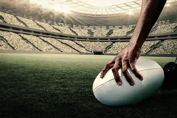 Cropped image of athlete holding rugby ball against rugby stadium