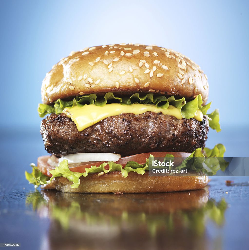 burger with melted cheese and sesame bun burger with melted cheese and sesame bun shot on blue background. Backgrounds Stock Photo