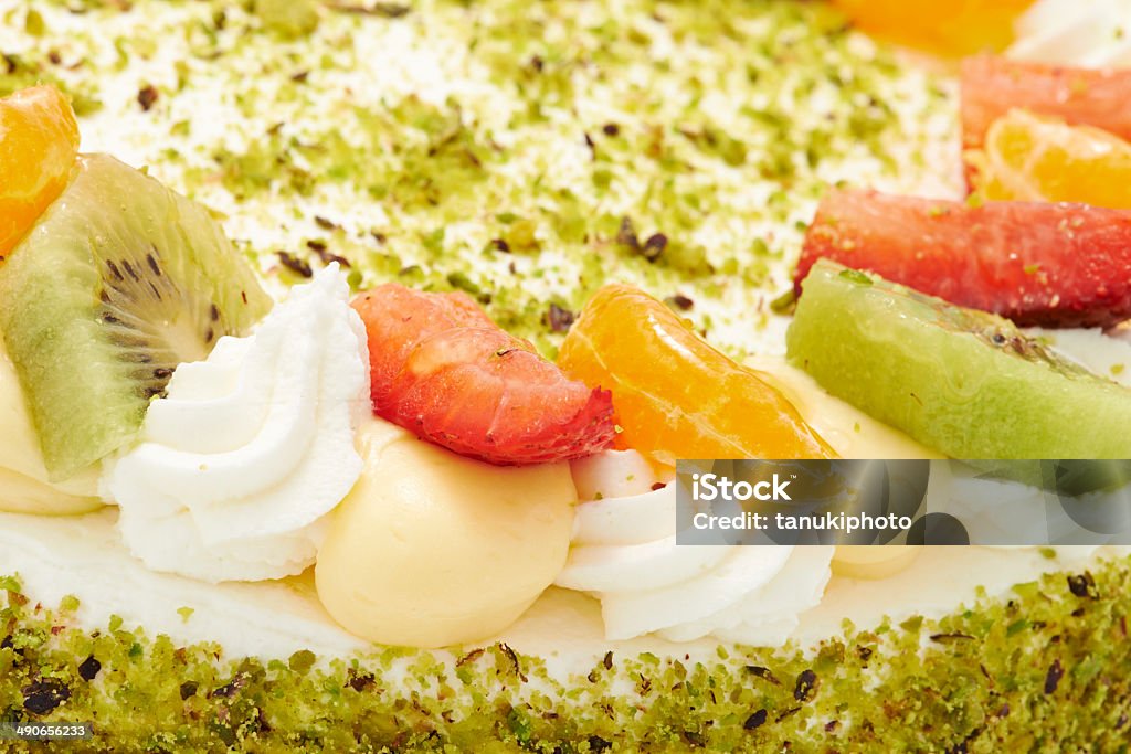 Gourmet Cake Close up of a sponge cake decorated with custard cream, whipped cream, strawberries, kiwi and tangerine slices. The side of the cake is decorated with chopped pistachio. Baked Stock Photo