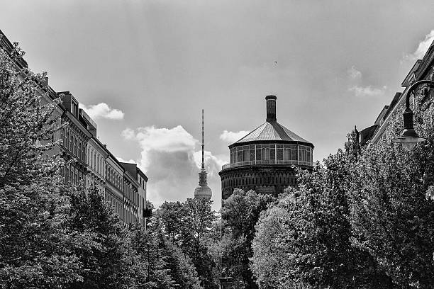 The TV Tower Berlin and Water Tower/ Prenzlauer Berg photographed from the view of a green avenue in black and white. The towers can be seen next to each other.  In the foreground an avenue with many trees.