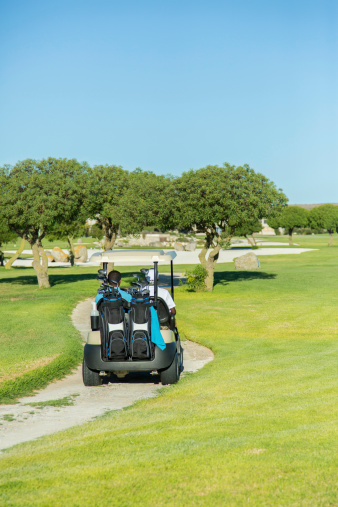 African golfers driving a golf cart on putting green, moving to their next location. Langebaan, Western Cape, South Africa 