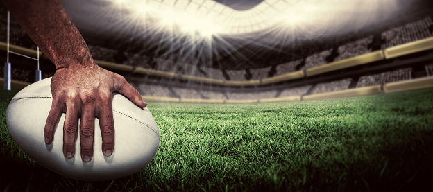 Close-up of sports player holding ball against rugby pitch