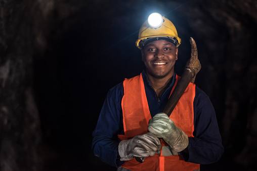 Happy African American miner working at a mine underground and wearing a helmet with a light
