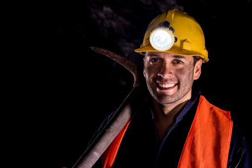 Happy man mining and wearing a helmet in a dark mine underground