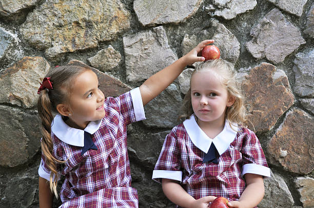 ragazza in equilibrio una mela su un altro ragazze testa. - old fashioned retro revival apple togetherness foto e immagini stock