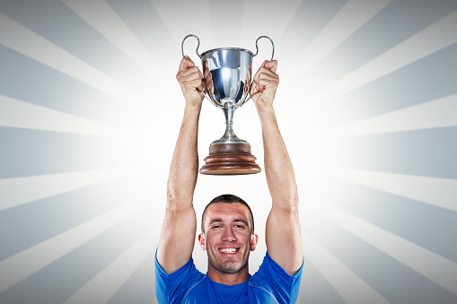 Portrait of smiling rugby player holding trophy against linear design