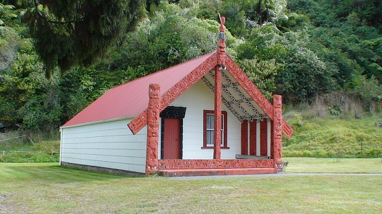 A Maori marae, or meeting house, situated in Rotorua , New Zealand with woodcarving and native bush behind.