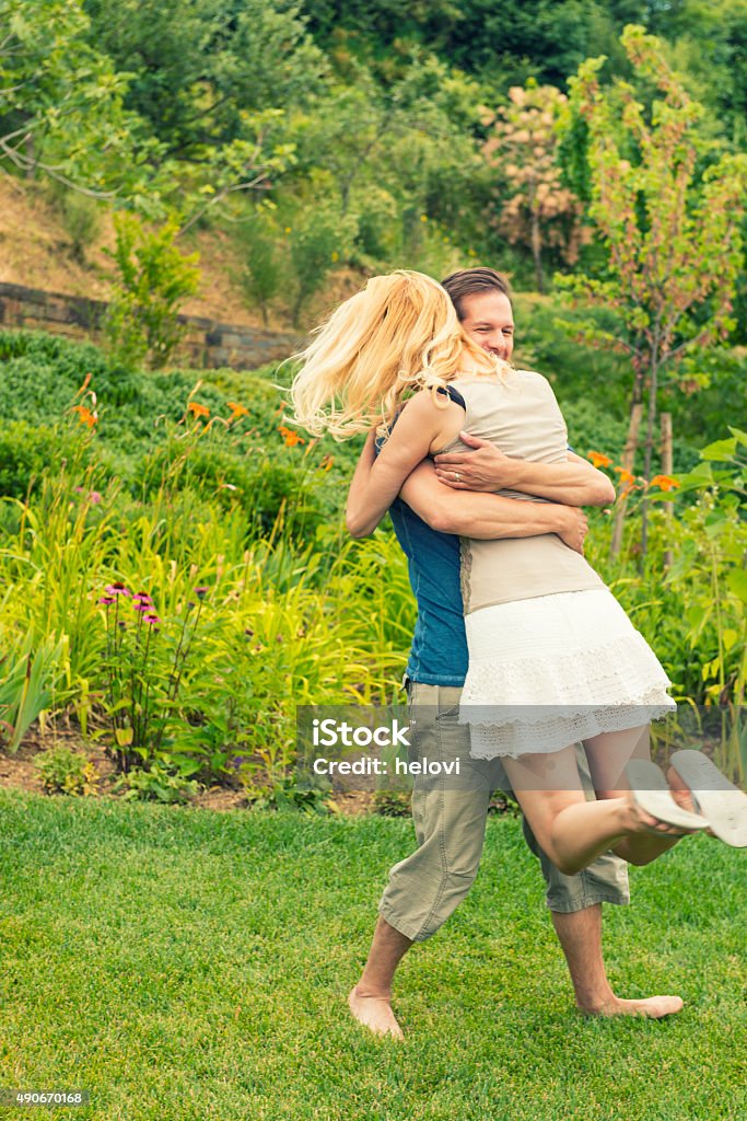 Young couple walking in garden Young couple, man and woman in love,  in the garden. Man holding woman in his hands and lifting her up happily. Summer time. Women has long blond hair, white short skirt. 2015 Stock Photo