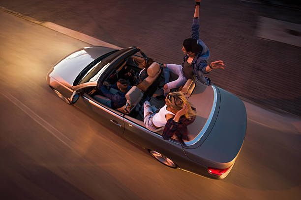 High angle view of group of young friends having fun on road trip in cabriolet. Blurred motion.
