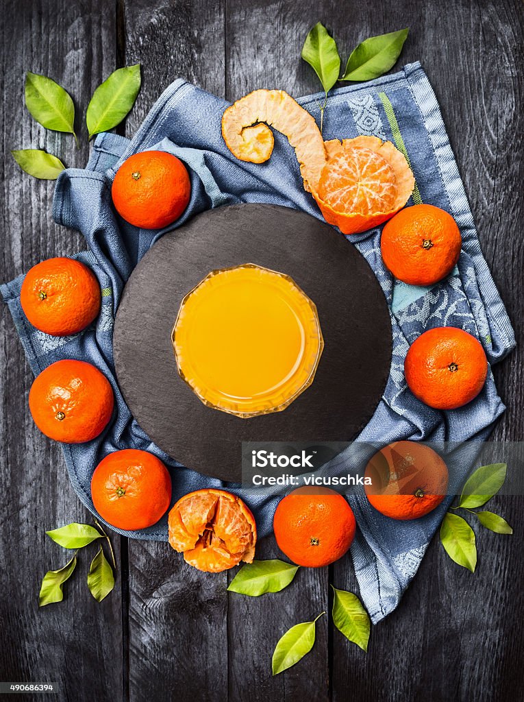 Fresh tangerines with leaves and glass of citrus juice Fresh tangerines with leaves and glass of citrus juice on blue wooden background, top view 2015 Stock Photo