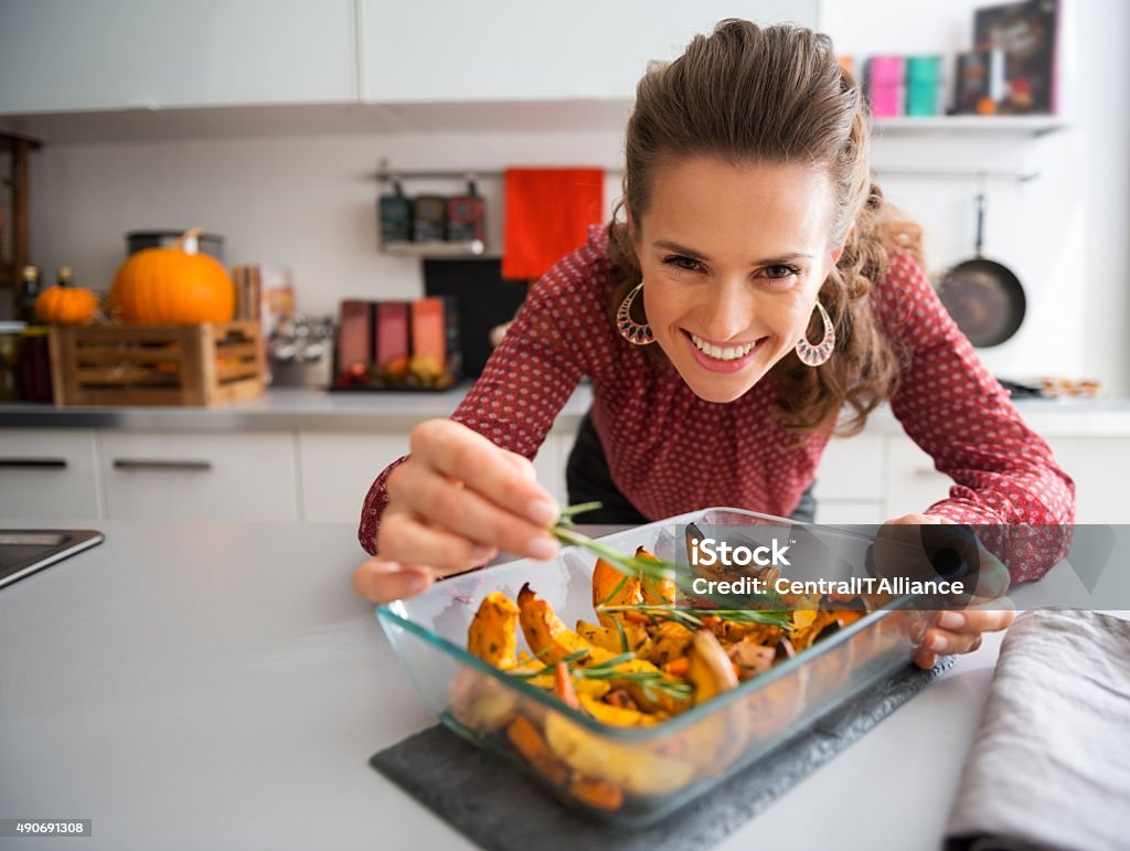 Smiling elegant woman preparing roasted pumpkin dish It's the touch of rosemary that counts, when you want to bring out the taste of roasted pumpkin. Cooking Stock Photo
