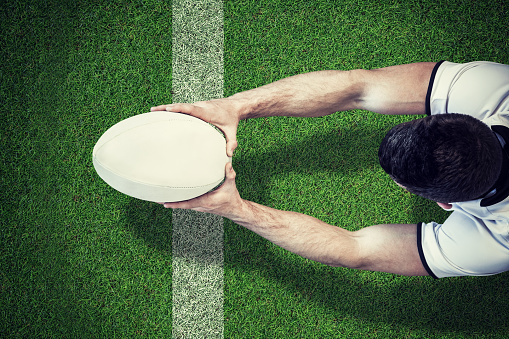 High angle view of man holding rugby ball with both hands against pitch with line