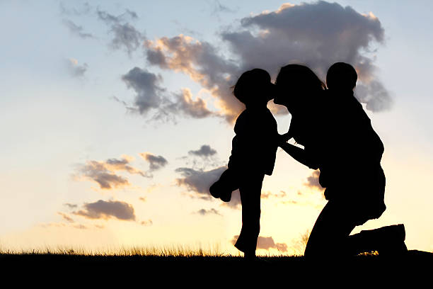 Mother with Two Young Children Hugging and Kissing the Silhouette of a mother and her two young children; a little boy and his baby brother are playing outside at sunset, hugging and kissing. group of people people recreational pursuit climbing stock pictures, royalty-free photos & images