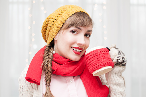 Portrait of an attractive woman wearing hat and scarf and holding a mug