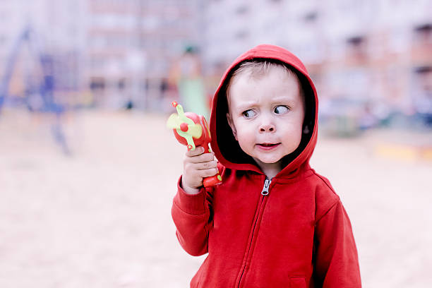 the boy made a funny face and squinted looking at toy gun