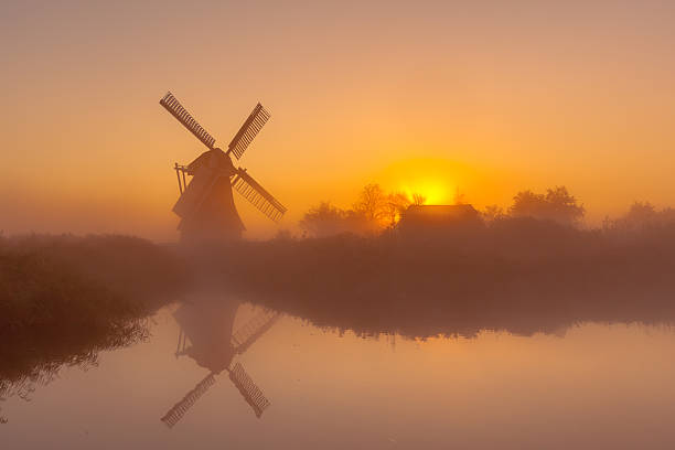 Historic windmill along a canal Characteristic historic windmill along a wide canal in a polder wetland on a foggy september morning in the Netherlands gouda south holland stock pictures, royalty-free photos & images