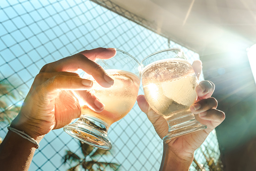 hands clinking beer glasses in summer sun backlight