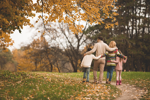 Rear view of a famila with two children walking together in the autumn park.