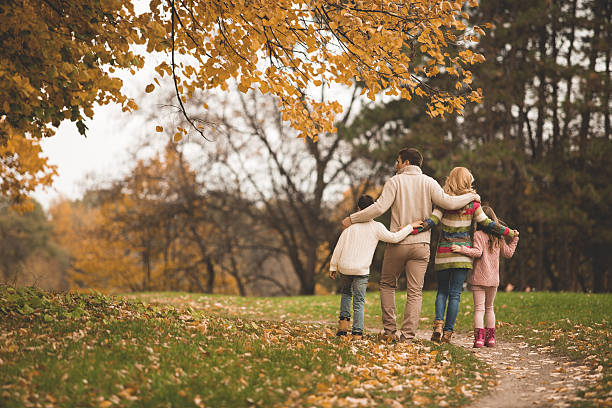 Family walking in the park Rear view of a famila with two children walking together in the autumn park. falling behind stock pictures, royalty-free photos & images