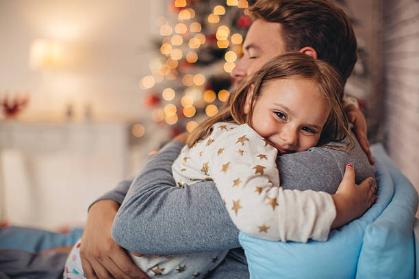 Father and his cute daughter in front of christmas three. Father and his cute daughter in front of christmas tree, lying on bed. Girl embracing daddy. family christmas stock pictures, royalty-free photos & images