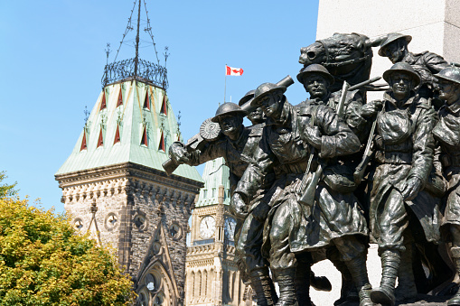 Ottawa, Canada - August 8, 2008: National War Memorial designed by Vernon March and unveiled by King George VI in 1939. The monument is composed of 23 bronze figures and a stone arch. In the background the Canadian Parliament building in downtown Ottawa, Ontario, Canada.