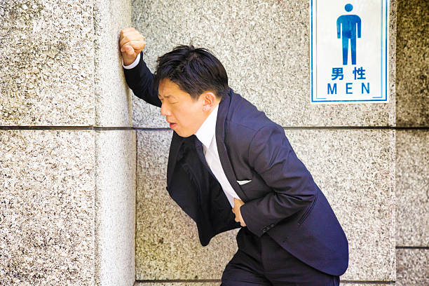 Sick Japanese businessman suffering stomach upset by public WC Sick Japanese businessman suffering stomach upset by public WC. He is holding his belly in pain. toilet sign in japanese style stock pictures, royalty-free photos & images