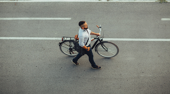 Young Businessman pushing his city bicycle. He has tattoos and hipster haircut. Riding city styles bicycle to and from work. Going home late from office. Top view.