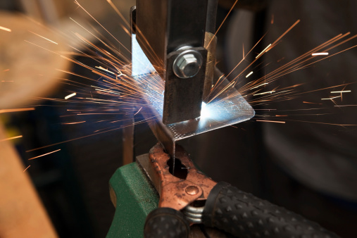 A MIG (Metal Inert Gas) wire feed welder is being used to join two pieces of steel. The base metal is held in a green vise, the foreground clamp is the ground connection for the welder.