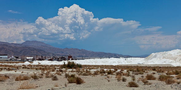 Salt beds on the shores of Searles Lake with industrial minerals mining buildings in the Mojave Desert beneath a massive cumulus cloud.