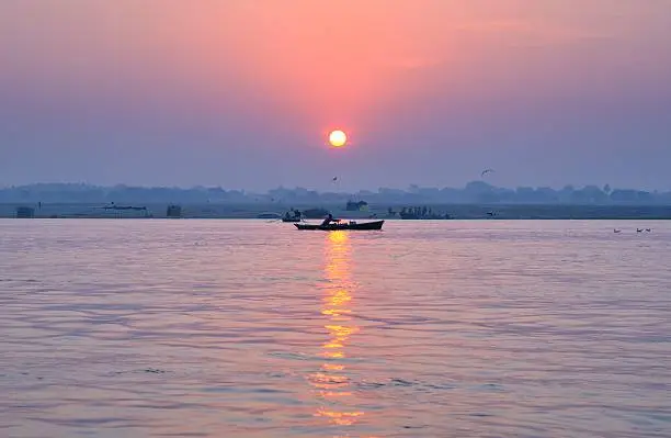 Sunrise on the Ganges River, Varanasi, India. A man paddles his boat.