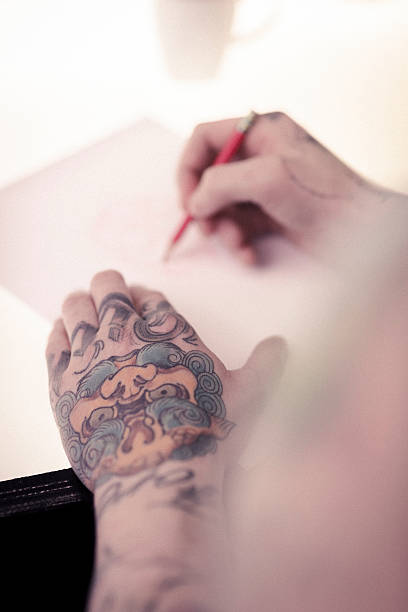 istock Artist's tattooed hands writing on paper 490748034