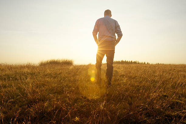 homme marchant dans la campagne environnante à la recherche au coucher du soleil - lonely man photos et images de collection