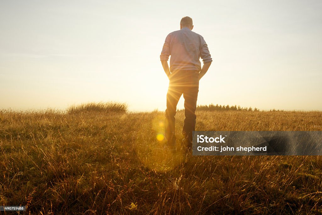 Man walking in the countryside looking at the sunset Man walking in the countryside looking at the sunset, strong lens flare from the late afternoon autumn sun. Men Stock Photo