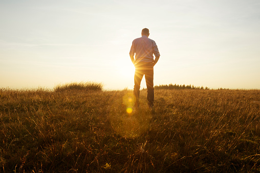 Man walking in the countryside looking at the sunset, strong lens flare from the late afternoon autumn sun.