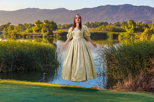 A beautiful young woman wearing a golden gown, floating in mid-air over a pond in the countryside. A great storybook adventure!