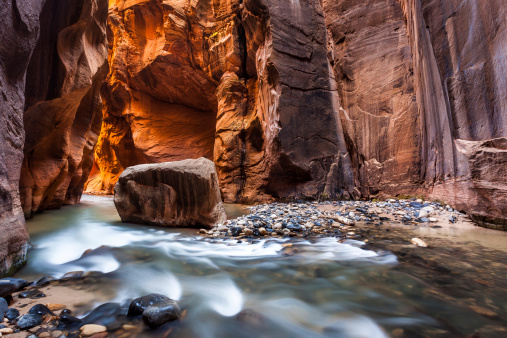 Two women walking in the river using walking sticks and carrying backpacks in the Narrows at Zion national park Utah