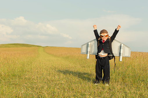 A young British boy is wearing a jetpack standing in a grass field and is ready to take everything about your business in the up direction.