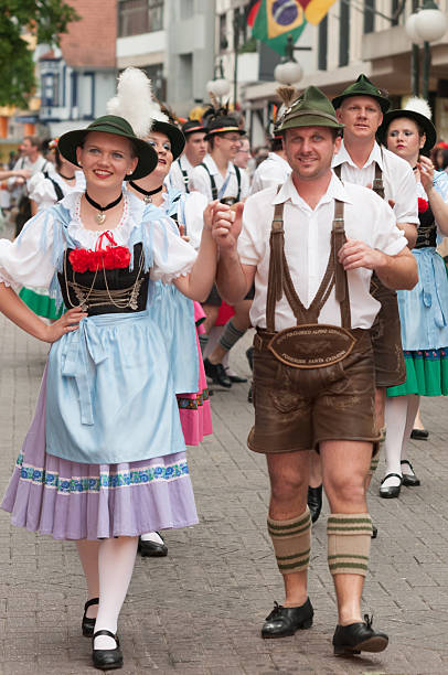 Blumenau, Santa Catarina, Brasil - October 15, 2011: A couple and the people from a German folk dance group walking down the street parade, in the heart of Blumenau to celebrate the Oktoberfest, along with buildings, a Brazilian and German flags in the background. 