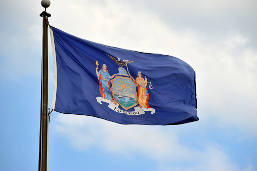 New York Flag flying in the wind with beautiful sky on the background.