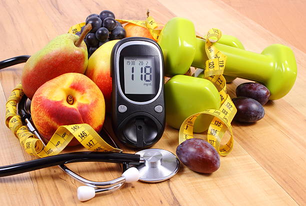 Glucose meter with medical stethoscope, fruits and dumbbells stock photo