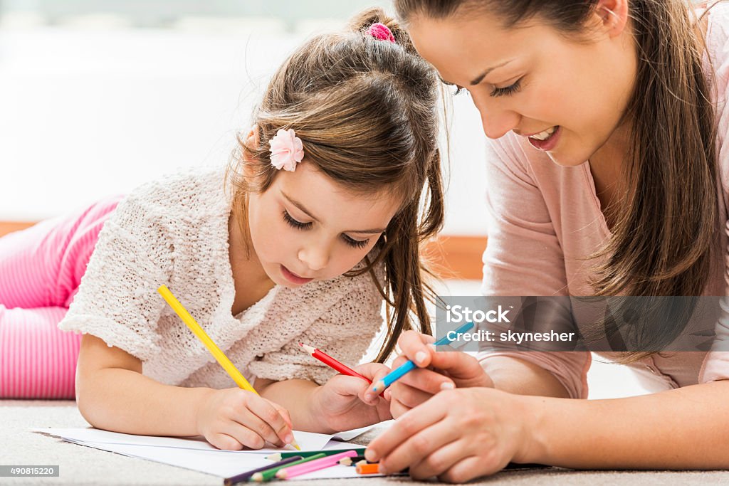 Smiling mother coloring with her daughter at home Young mother drawing with her little daughter while lying down on carpet at home. Coloring Book - Art Supply Stock Photo