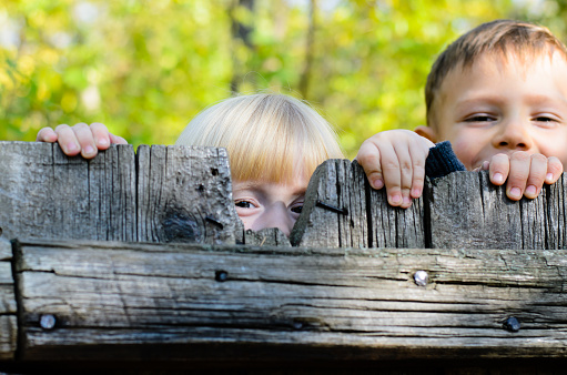 Two boys sitting on a wooden fence looking at camera and holding ball