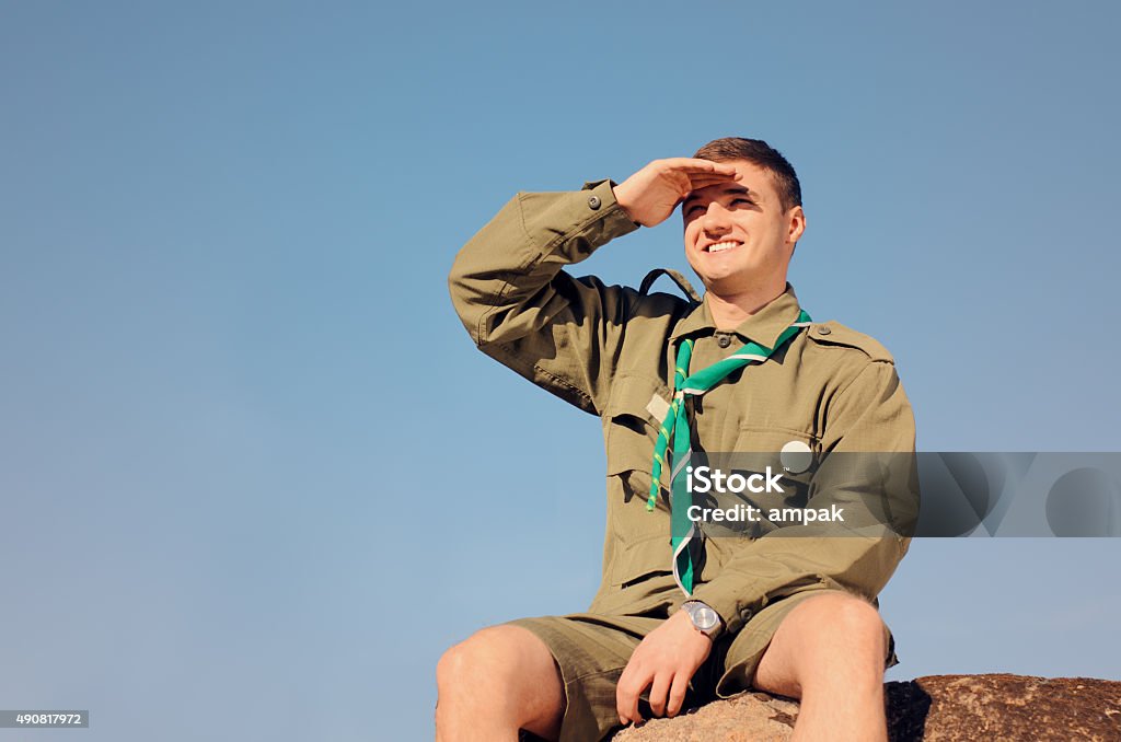 Boy Scout sentado en Rock frente al campo - Foto de stock de Boy scout libre de derechos