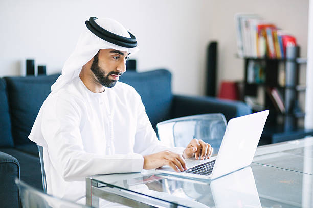 contenido arab hombre usando una computadora portátil en su hogar - istockalypse fotografías e imágenes de stock